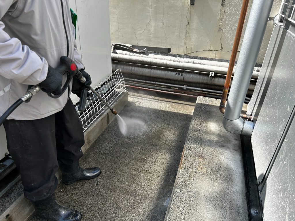 シリカテック施工前に、屋上設備まわりのコンクリート床を高圧洗浄機で洗浄し、表面の汚れや油分を除去している様子