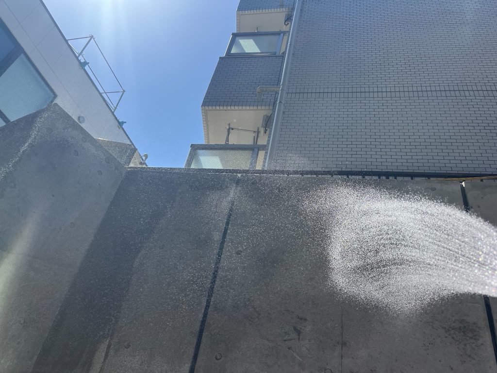東京都練馬区の新築集合住宅のコンクリート打ちっぱなしの外壁。シリカテック散布後の残材を水で洗い流している様子。