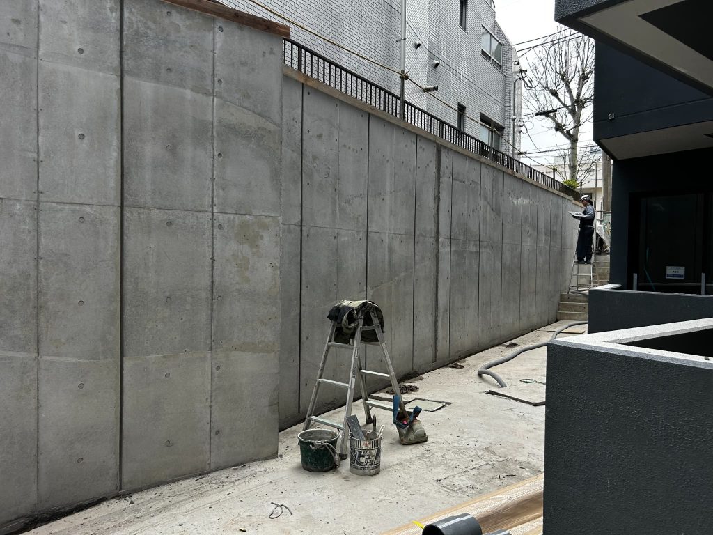 東京都練馬区の新築集合住宅のコンクリート打ちっぱなしの外壁。最後に水性塗料でコンクリート面の色合わせを行っている様子。