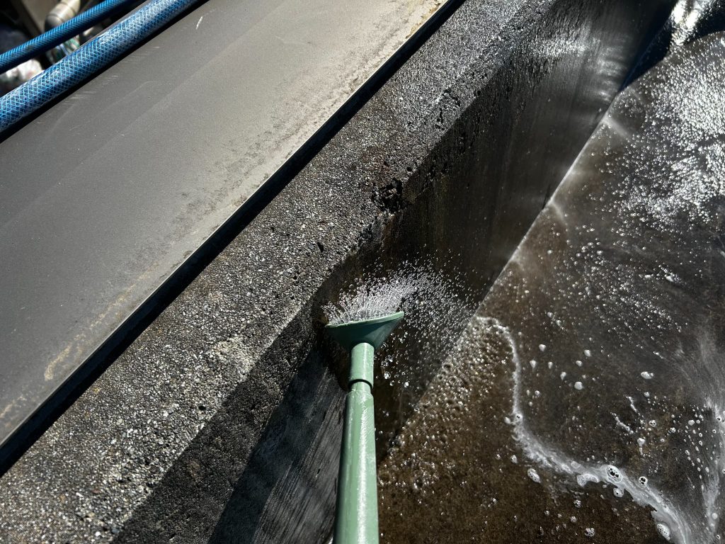 屋上のコンクリート表面に洗浄剤を散布し、10年ぶりの再防水工事に向けた下準備をしている場面