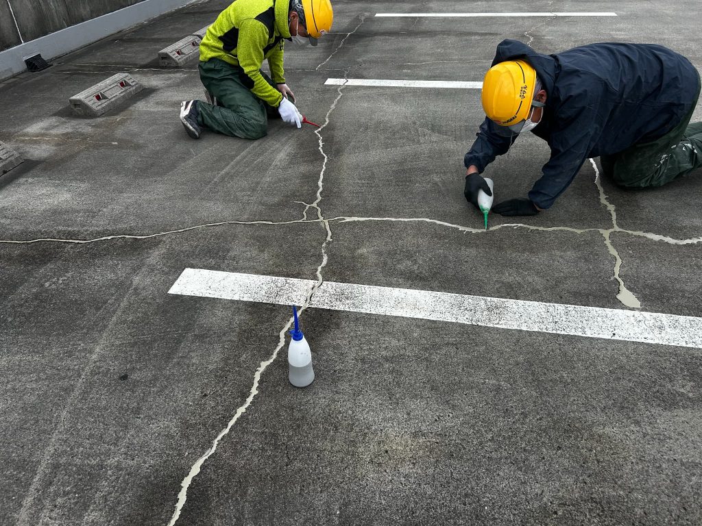 東京都府中市のショッピングモールの立体駐車場。屋上のひび割れ部分にセメント系グラウト材を注入している様子。